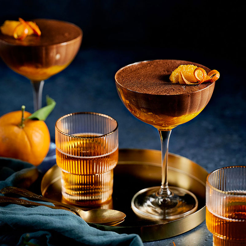 Mousse chocolat, orange et miel dressée à table, mise en scène avec verres et agrumes.