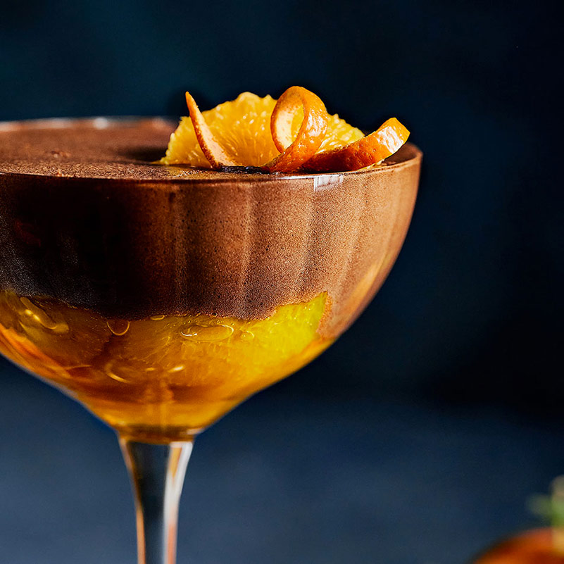 Vue de profil d’une coupe de mousse chocolat orange, avec les suprêmes pochés visibles au fond.