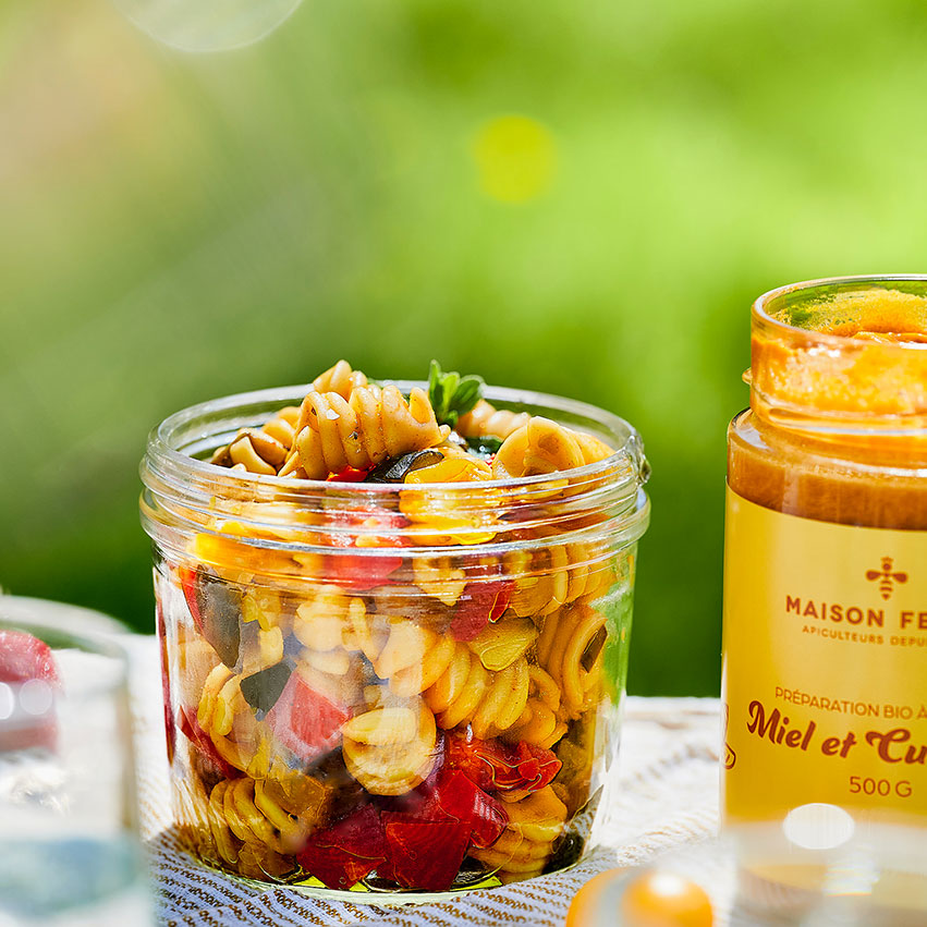 Un bol avec la salade de pâtes et légumes d'été avec le pot de miel et curcuma.