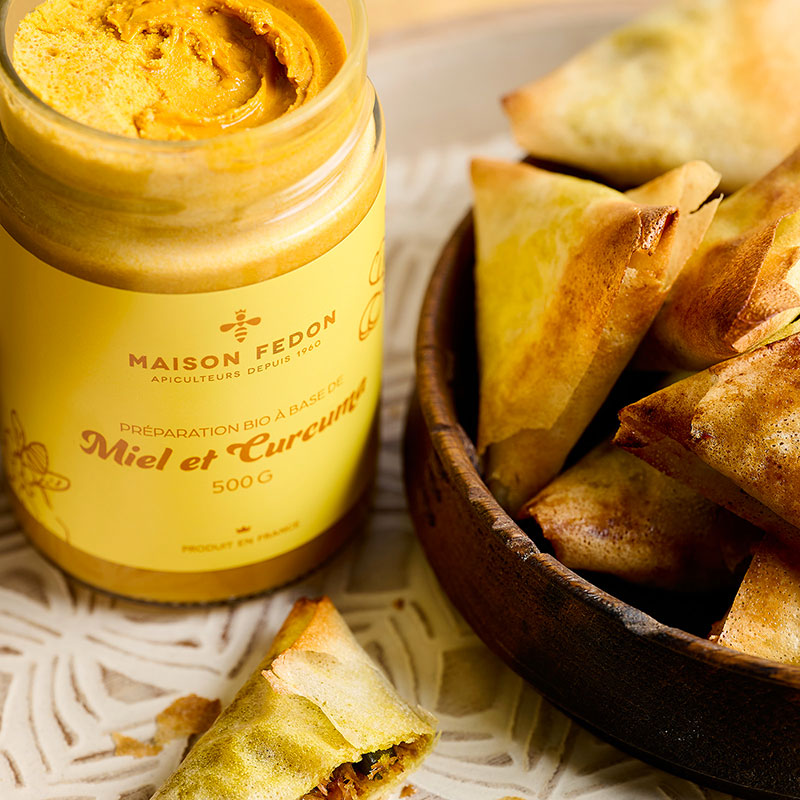 Pot ouvert de miel et curcuma Maison Fedon avec des samoussas.