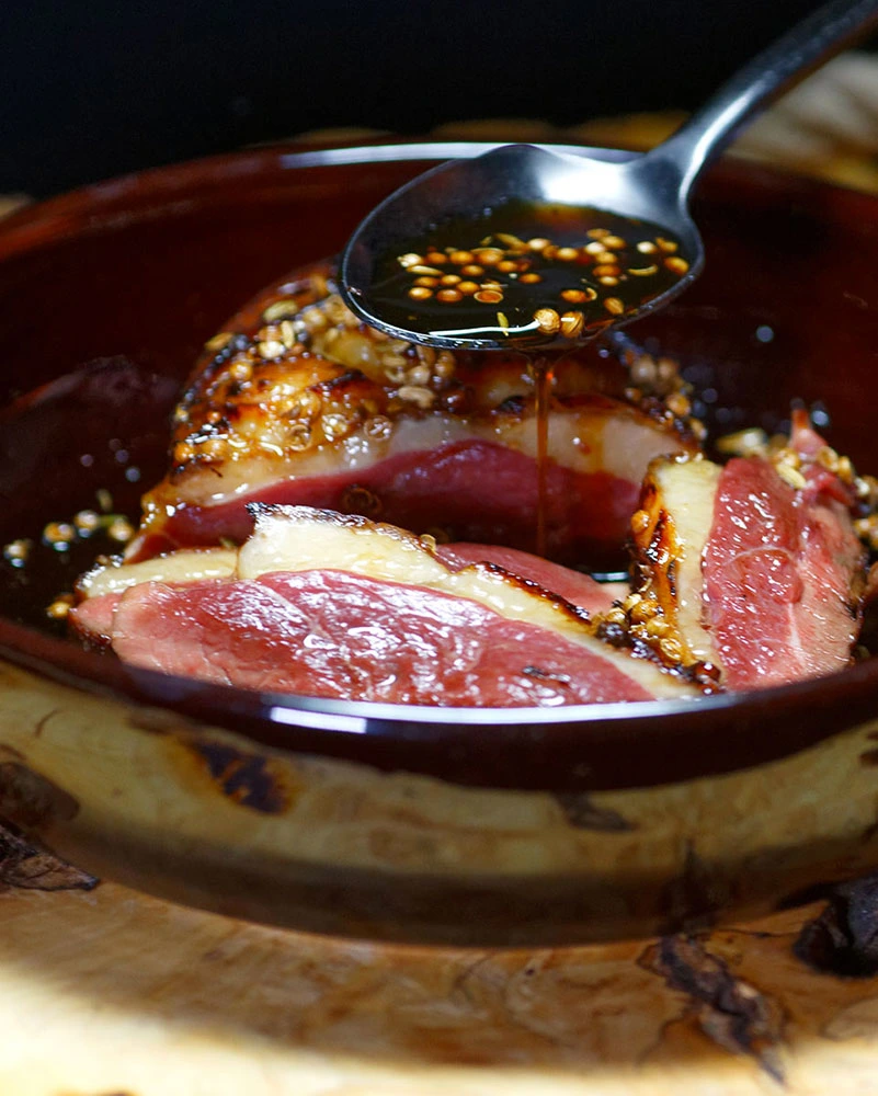 Tranches de magret de canard et une cuillère avec la sauce au miel et aux épices.