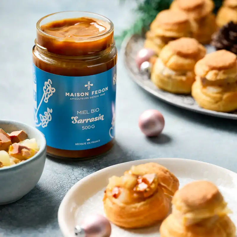 Un pot de miel bio de sarrasin Maison Fedon avec des choux apéritif garnis sur des assiettes.