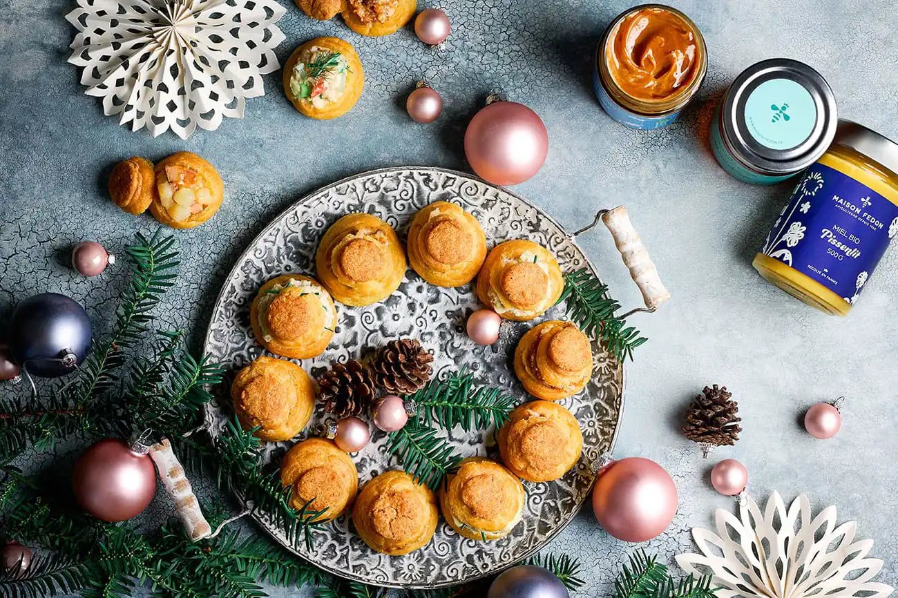 Vue de dessus d'une table de fêtes de fin d'année avec une couronne de choux apéritif, trois pots de miel et quelques décorations.
