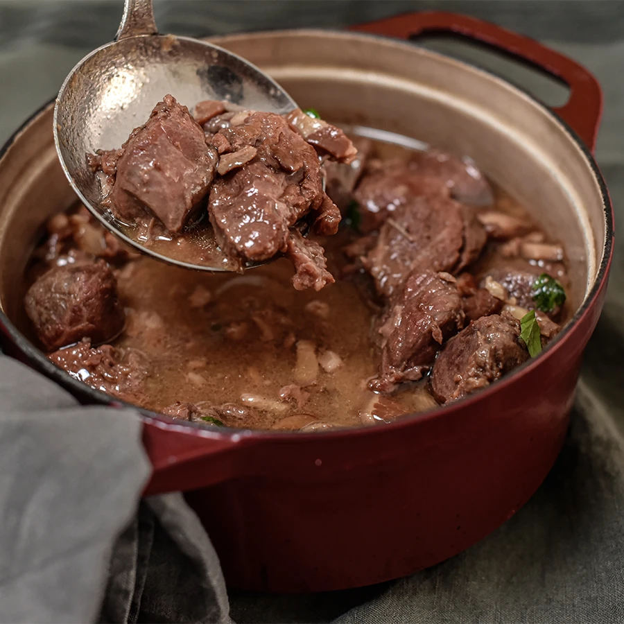 Vue rapprochée de la joue de porc à la bière et au miel dans une cocotte rouge en fonte.