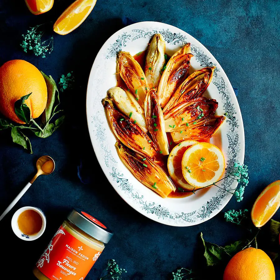 Endives braisées au miel et à l’orange, présentées sur une assiette avec des rondelles d'agrumes.