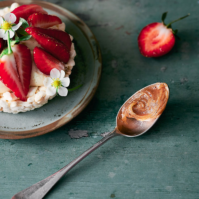 Gros plan sur une tartelette aux fraises et une cuillère nappée de miel & noisette.