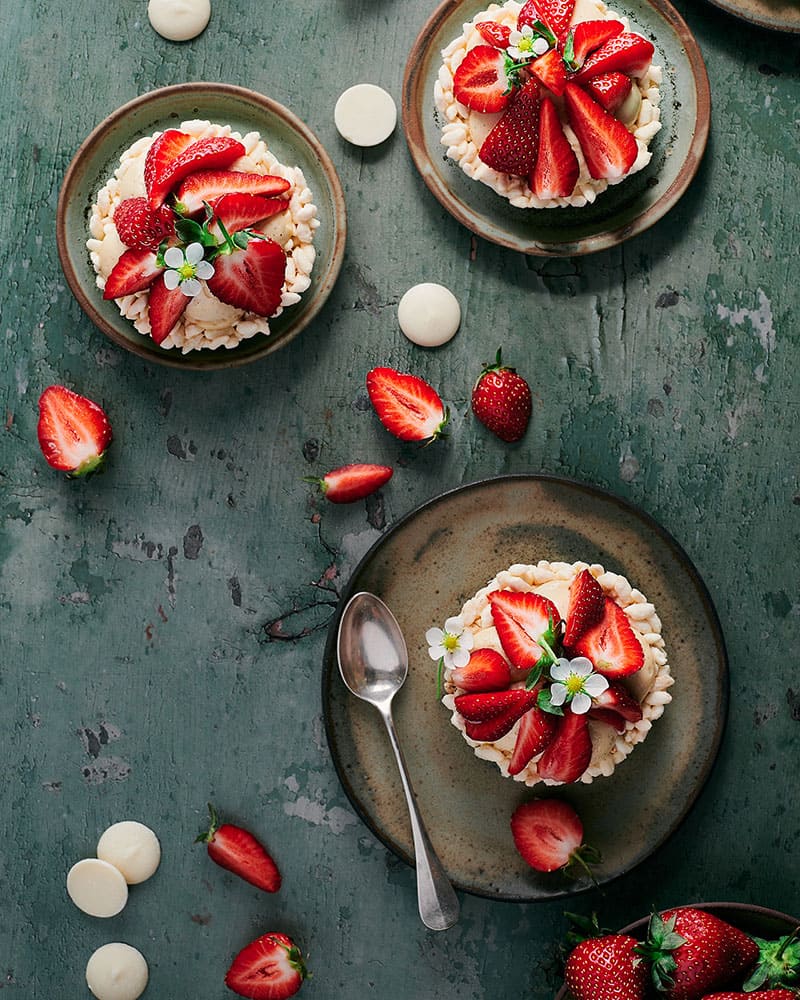Tartelettes aux fraises et miel-noisette vues du dessus, servies dans des assiettes avec des fraises fraîches et des morceaux de chocolat blanc.