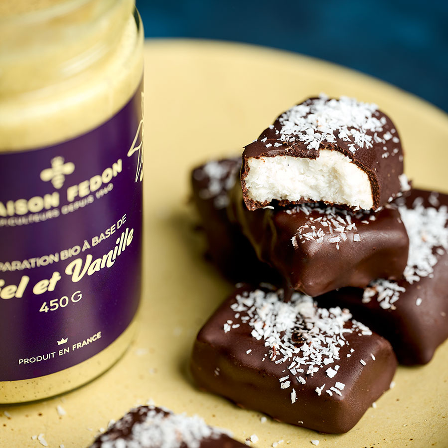Gros plan sur des Bounty maison saupoudrés de noix de coco râpée, avec leur garniture blanche et leur enrobage de chocolat noir.
